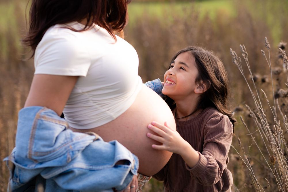 Candid maternity moment captured in natural outdoor setting with warm lighting.