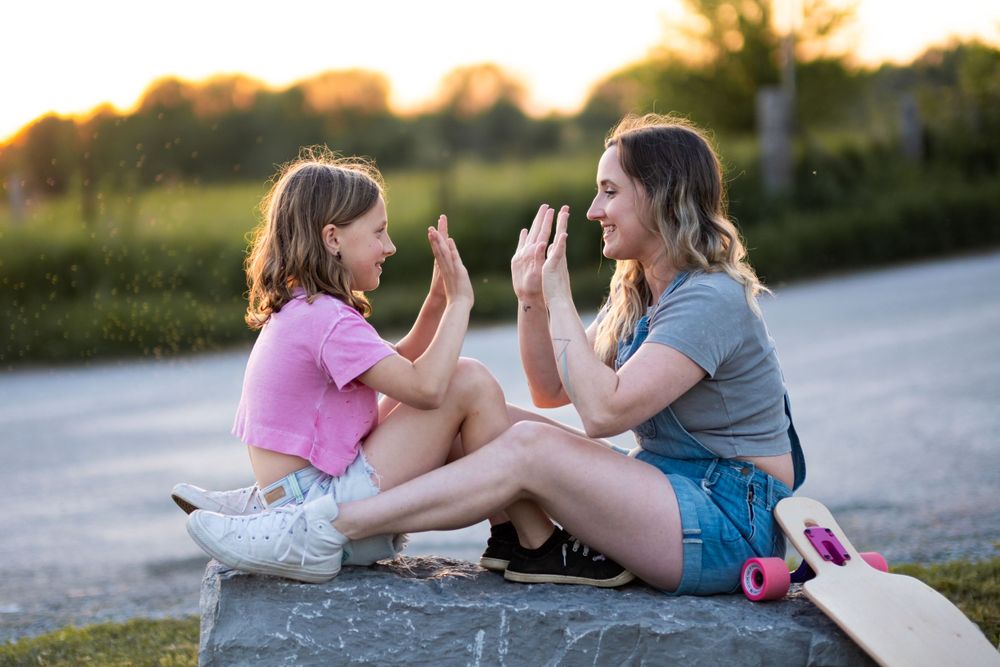 Mom and child playing and laughing together on rocky beach at sunset.