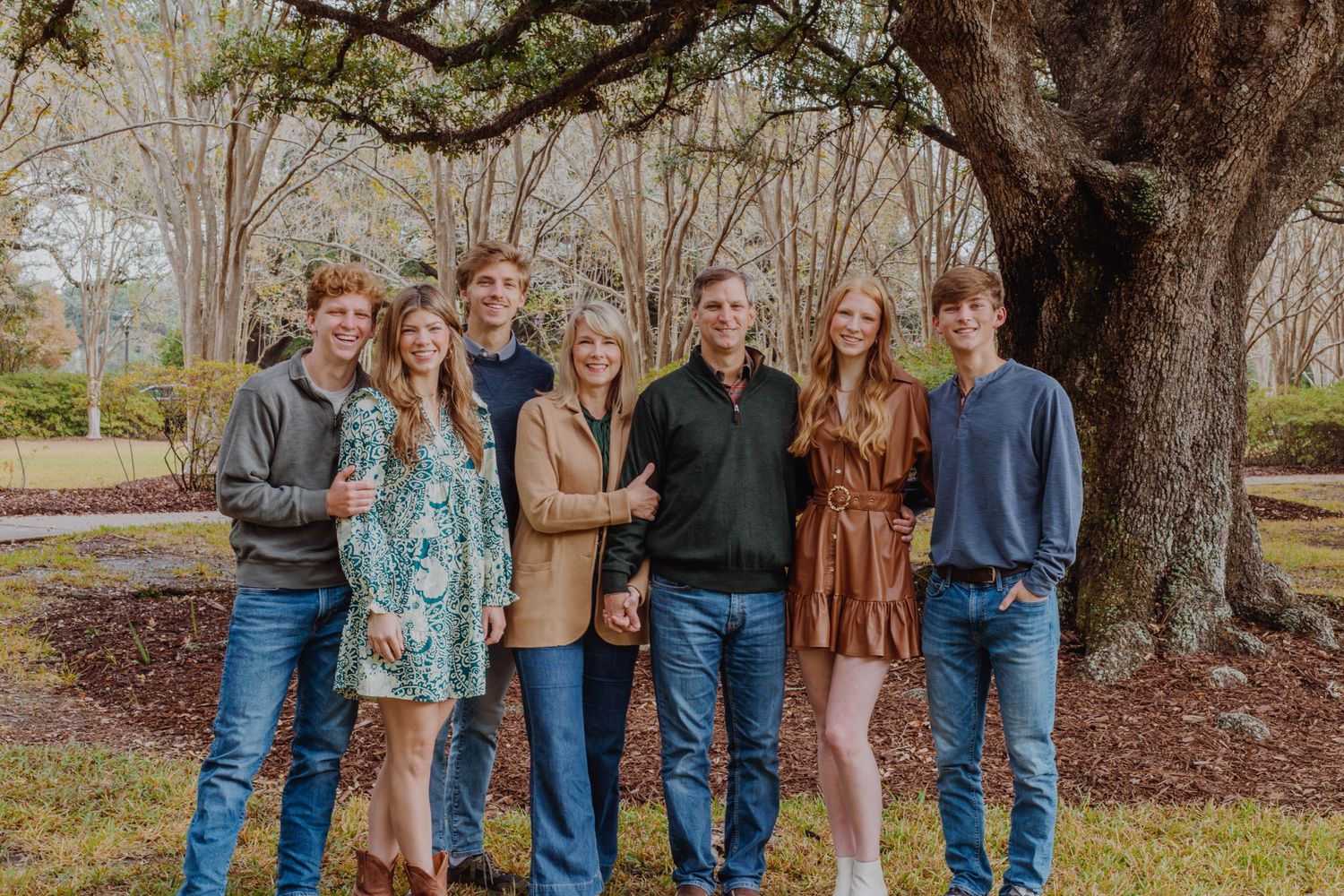 Group portrait of family members standing together beneath a large tree outdoors.