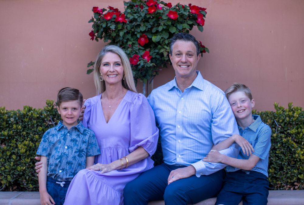 Happy family of four posing together in front of red roses and a terracotta wall.