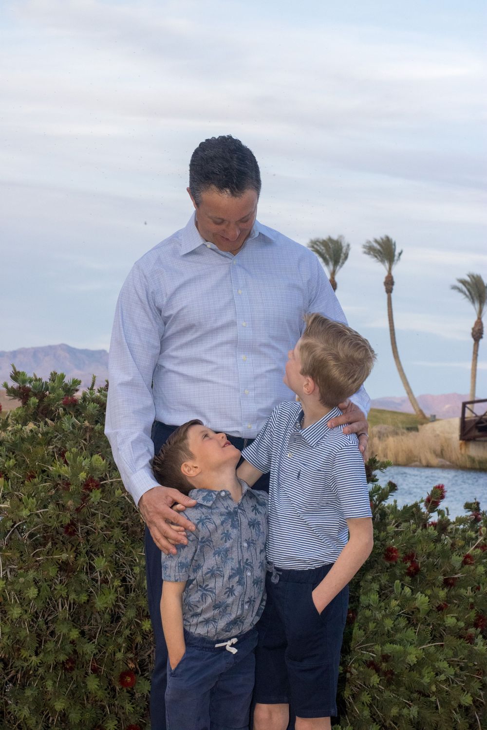 Father lovingly interacting with his two young sons outdoors near a scenic waterway.