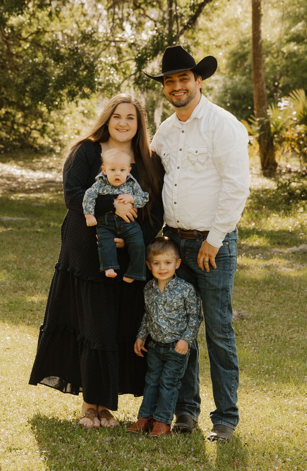Young western family posing outdoors, parents in black and white with two young boys in coordinated country attire.