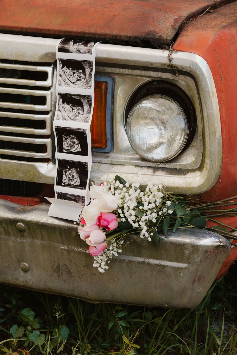 Vintage red truck bumper displays baby ultrasound strip and pink floral bouquet for maternity announcement.