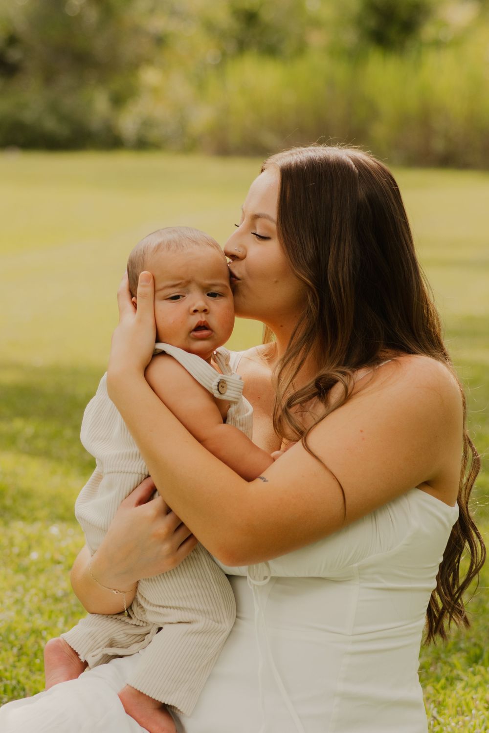 A tender moment between parent and child playing together in a sunny green field on a warm afternoon.