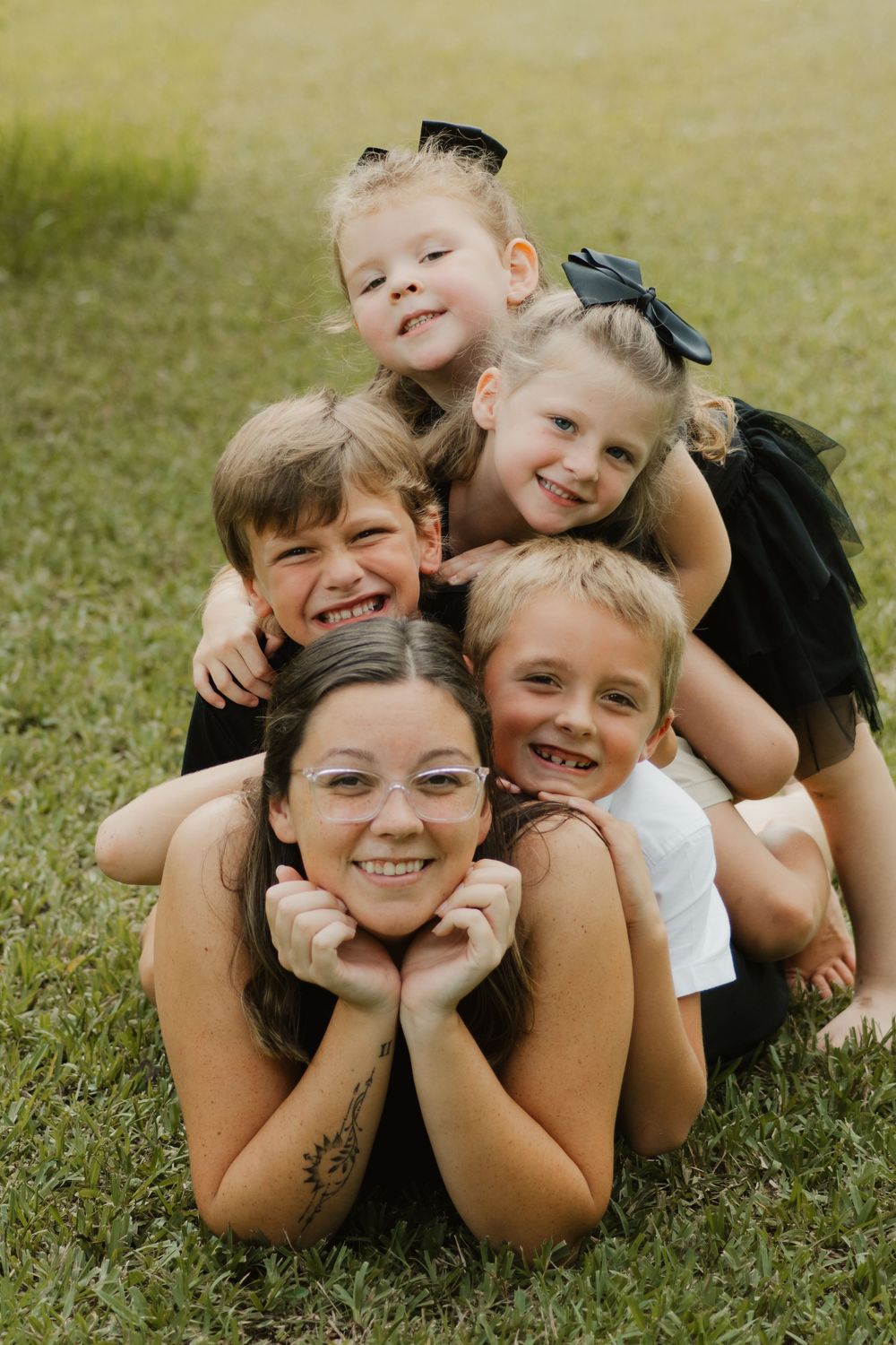 A playful group lies in green grass making silly faces and poses in a progressive series of candid shots.