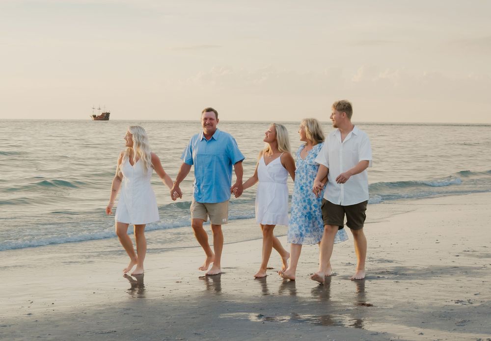 Family of five walking hand-in-hand along a sandy beach at sunset with calm ocean waves.