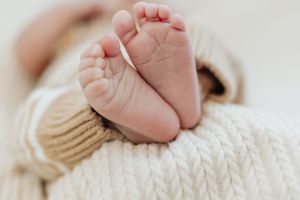 Close up of tiny baby feet resting on cozy white knitted blanket.