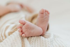 Delicate newborn toes and feet against soft white knitted texture.