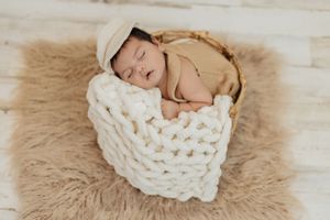 Infant sleeping on beige fur rug with white chunky knit blanket.