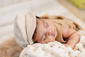Sleeping newborn swaddled in white blanket on soft textured backdrop.
