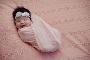 Baby resting on pink lace textured blanket in soft lighting.