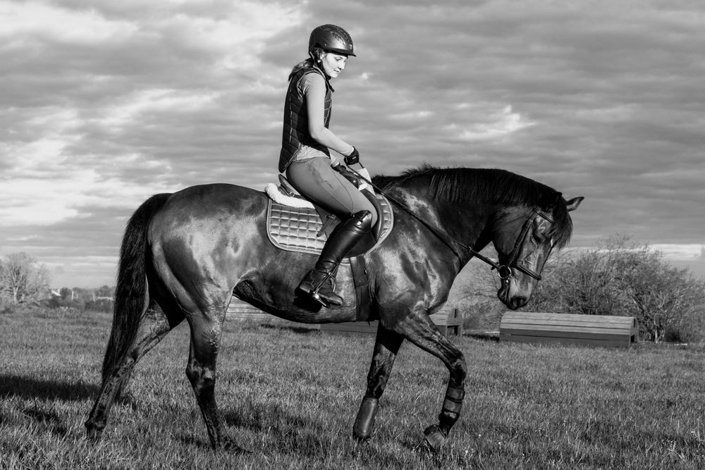 Black and white action shot of horse and rider galloping across grassland.