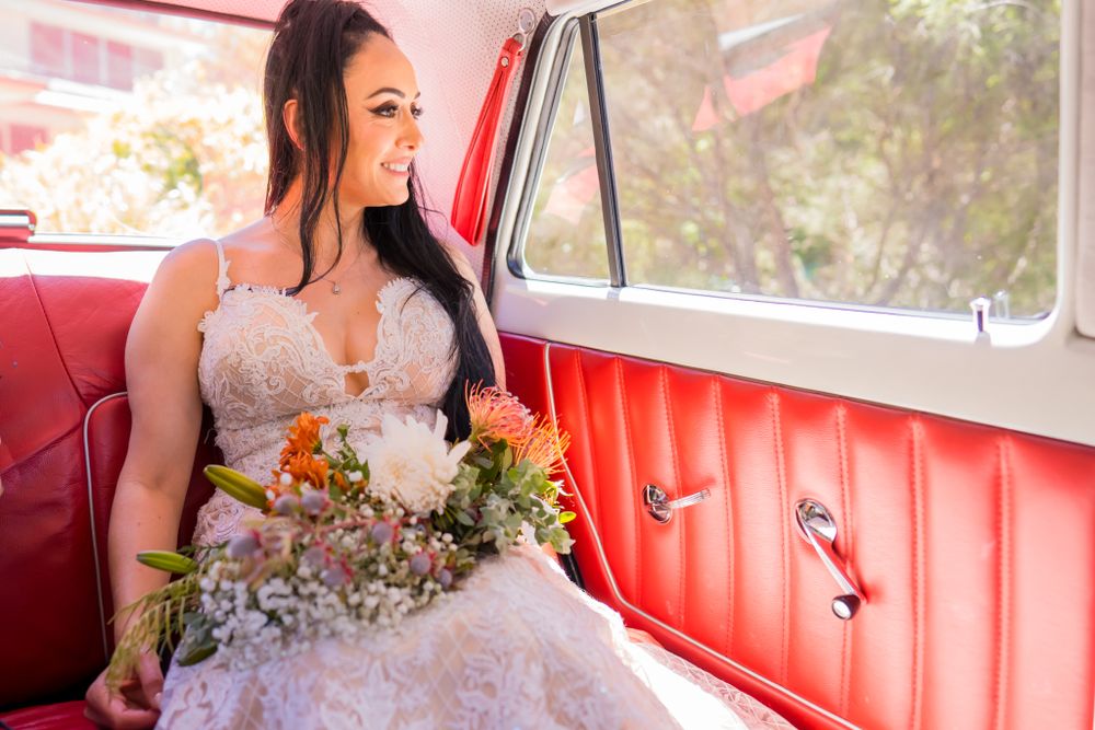 Wedding party member sitting in classic car with red interior holding floral bouquet.