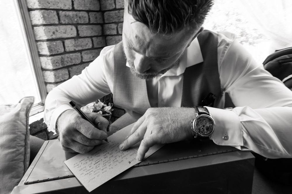 Black and white image of someone writing on paper while wearing formal attire.