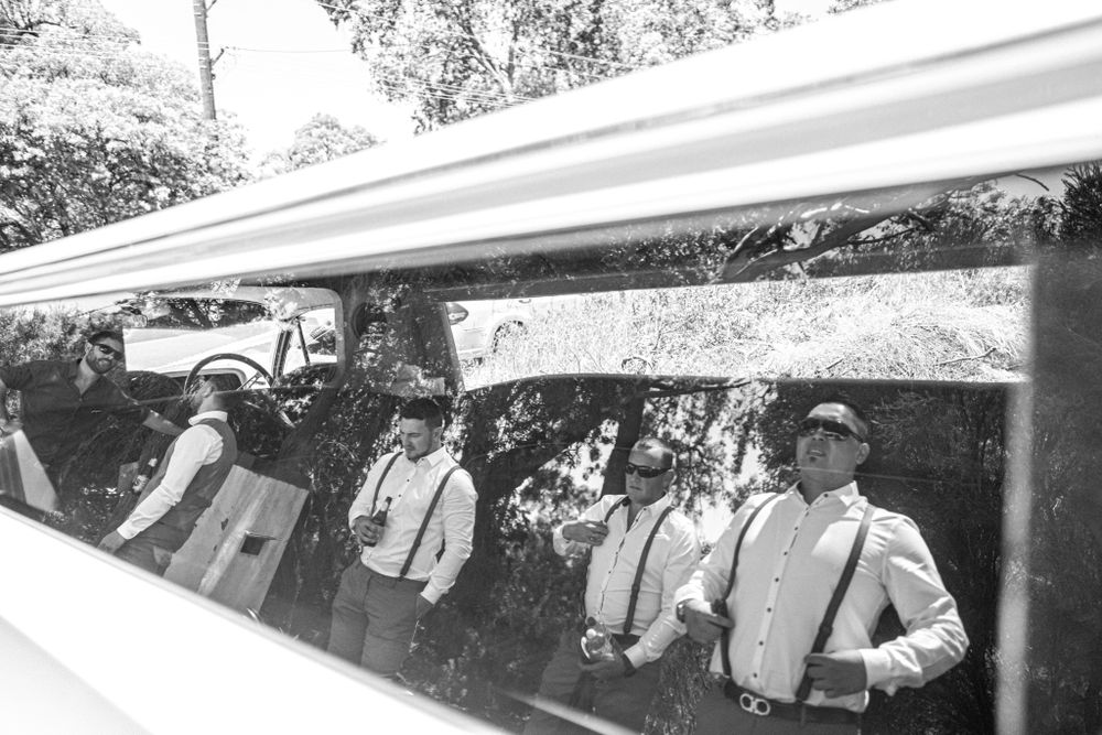 Black and white reflection of groomsmen in car window.