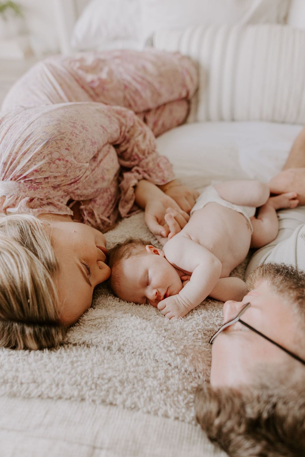 A tender family moment on a plush carpet as they lay together with their newborn baby.