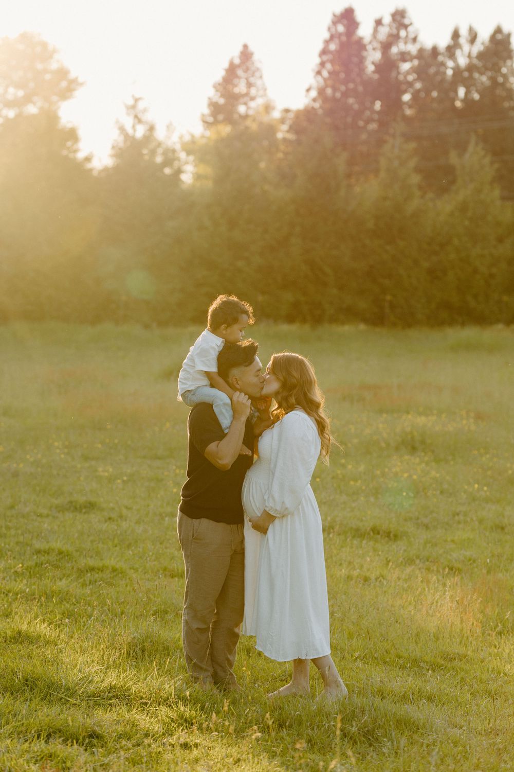 Family shares tender moment in grassy field during sunset.