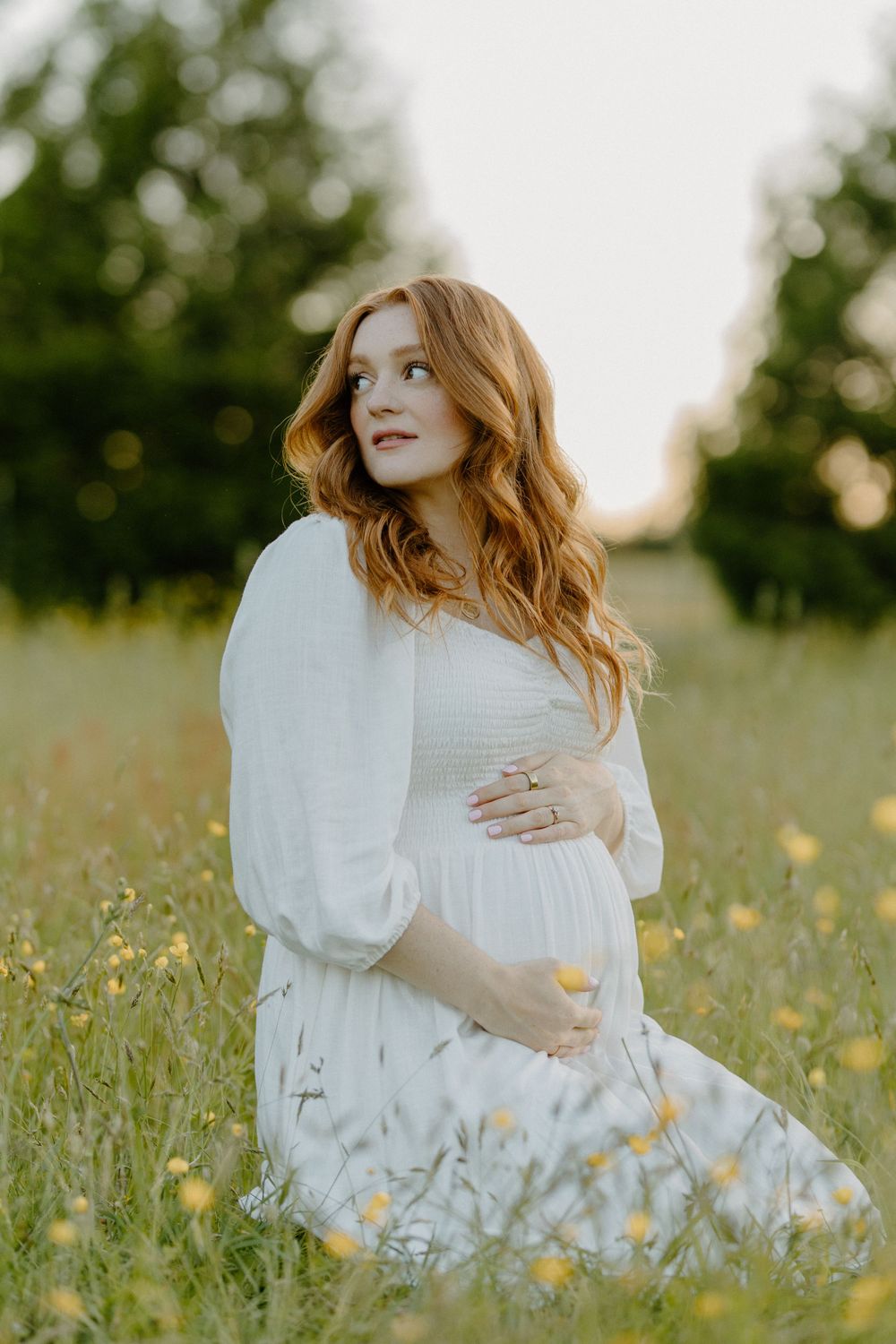 Person in white dress poses in wildflower meadow during maternity photoshoot.