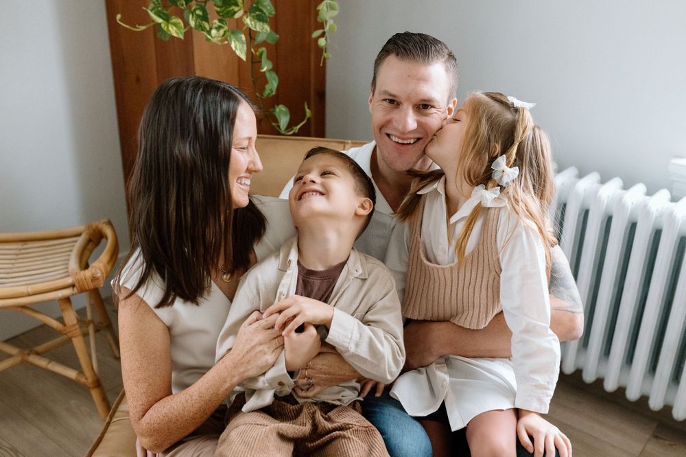 A happy family laughs together while sitting on a couch next to a radiator.