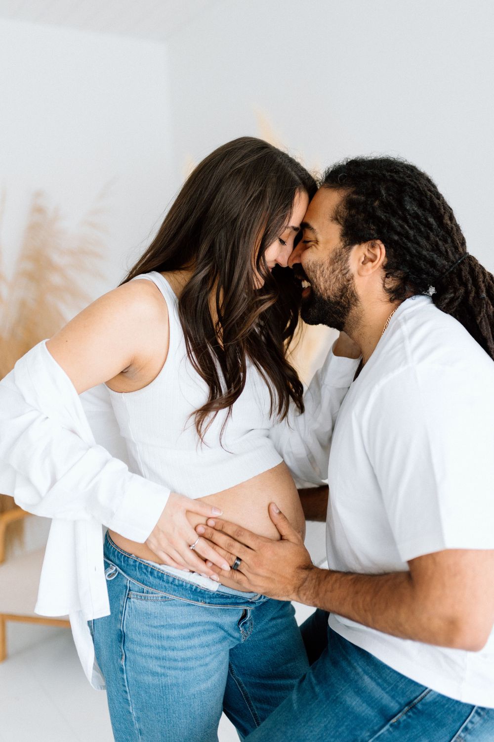 An expectant couple shares an intimate moment in a bright white room.