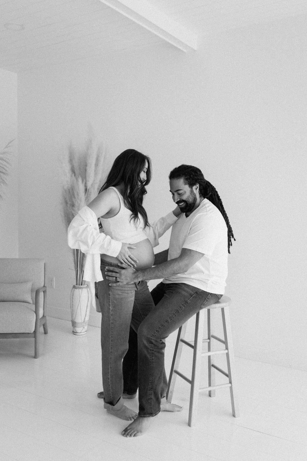 A couple sitting together in a minimalist white room during a maternity photoshoot.