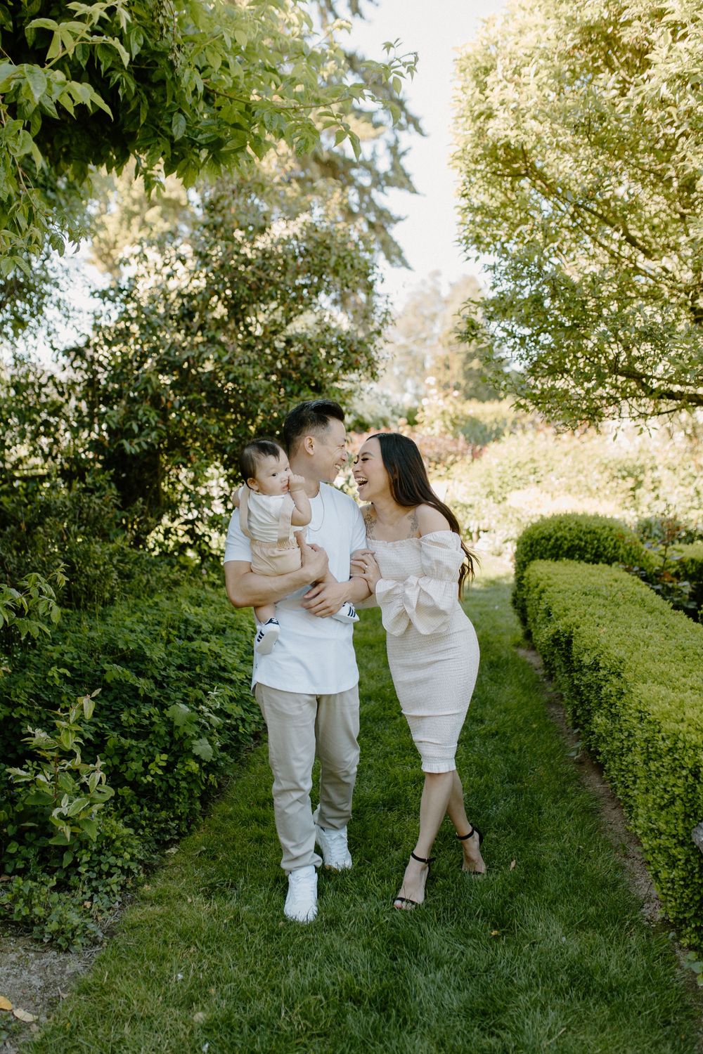 A sweet family moment captured on a garden path lined with manicured hedges and lush greenery.