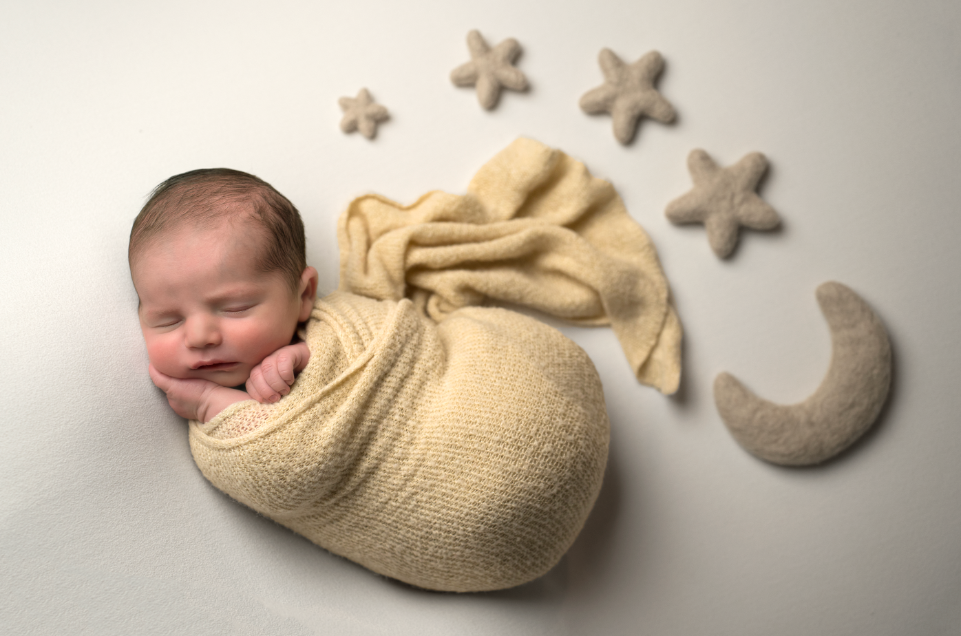 Newborn baby swaddled in cream wrap sleeping peacefully, surrounded by star and moon props on white background. Embracing Life’s Beauty