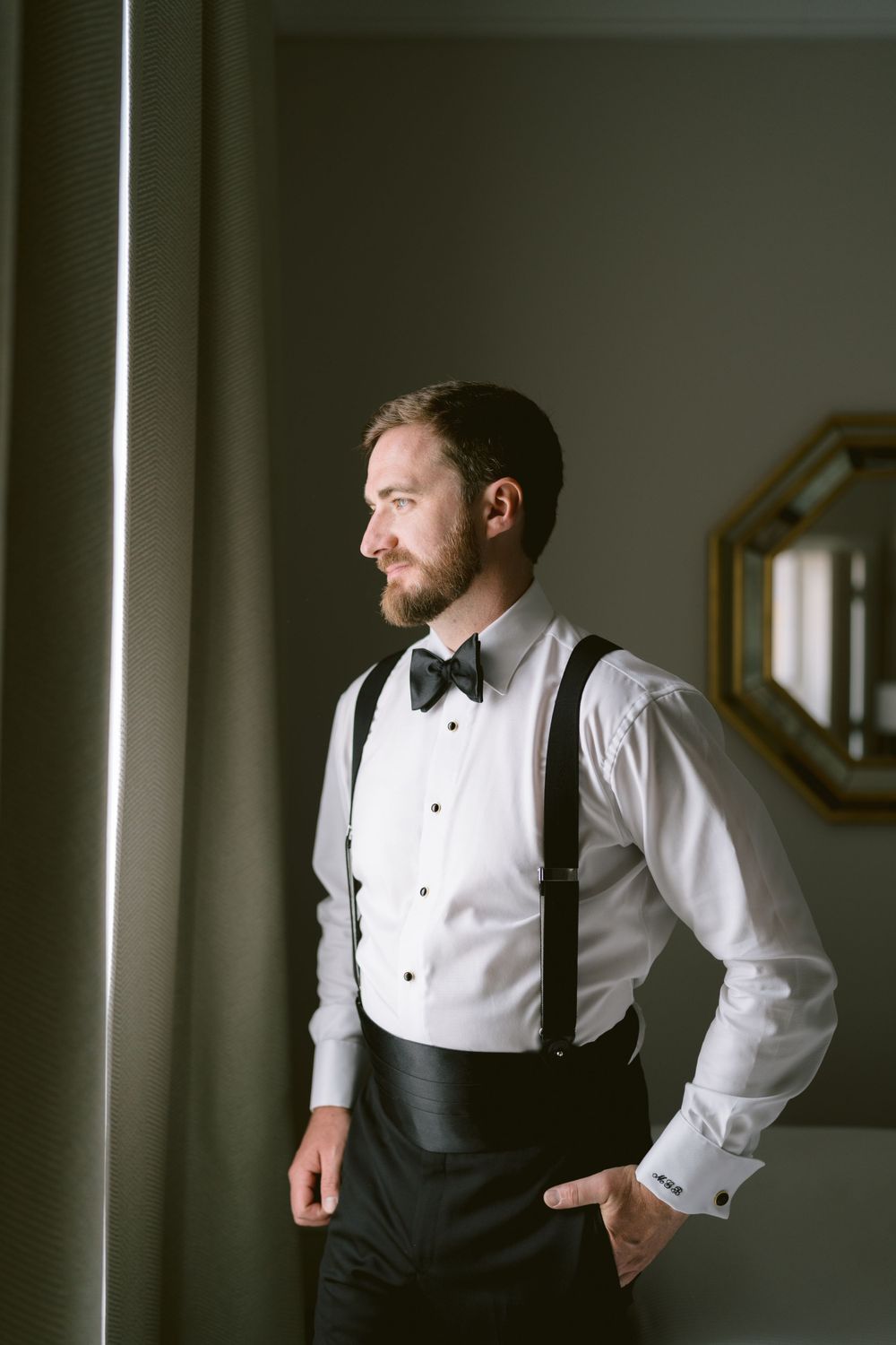 Groom in classic tuxedo and suspenders poses in dramatic lighting. Photoshoot by Venice Photographer Alina Indi