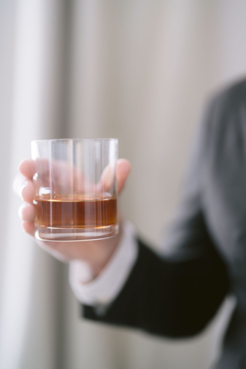 Hand holding a glass of whiskey against a light background.