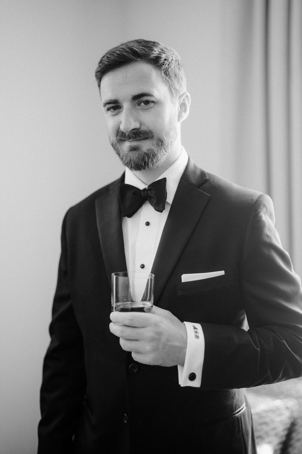 Man in tuxedo and bowtie holding a glass of whiskey in black and white photography. Photoshoot by Venice Photographer Alina Indi
