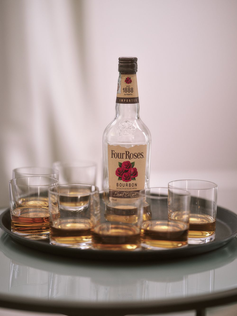 Several glasses of bourbon and whiskey bottles arranged on a dark serving tray.
