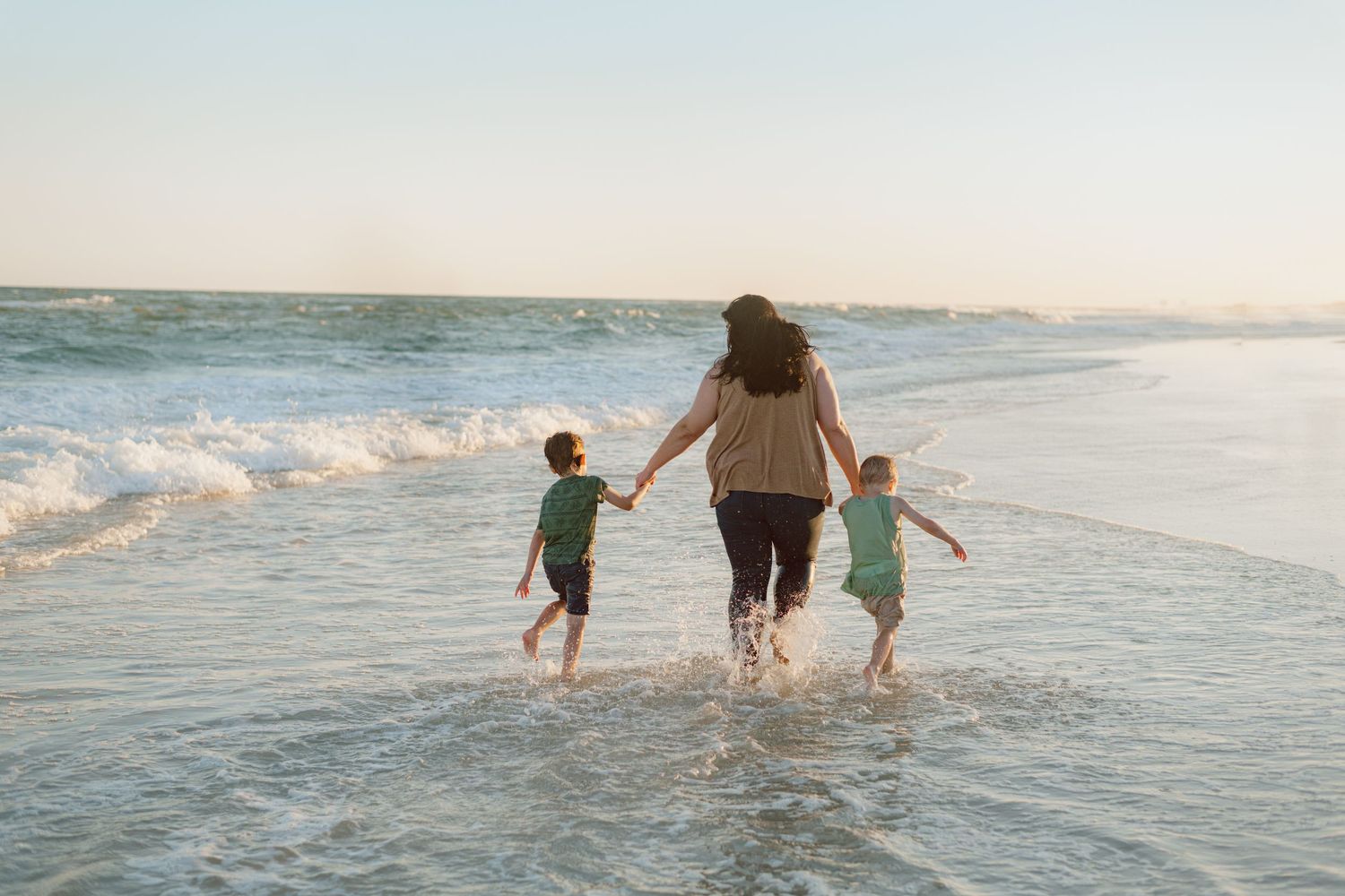 Parent and children holding hands while splashing in ocean waves at sunset.