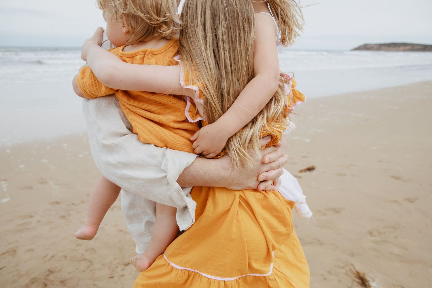 An intimate embrace between family members wearing orange and white clothing on a beach.