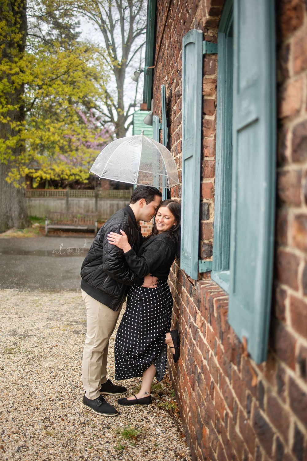 Romantic couple embracing under umbrella by brick building window.