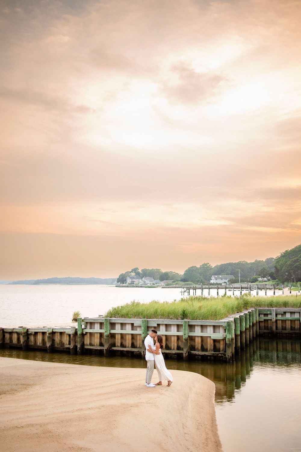 A person walks along a peaceful coastal boardwalk during a dreamy pink sunset over the water and distant hills.