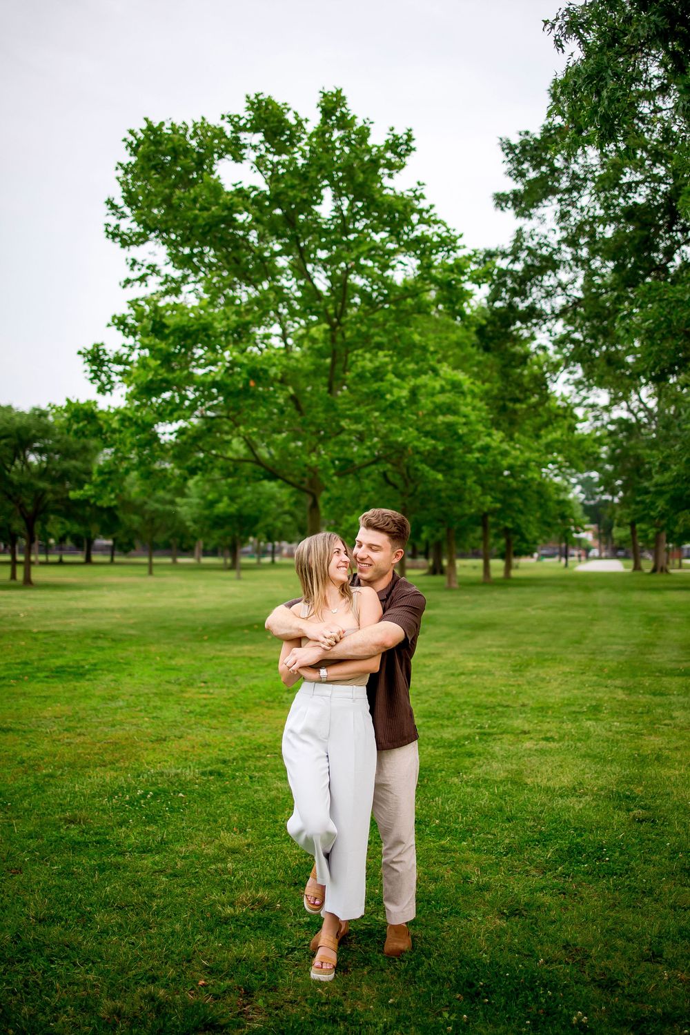 A couple embraces romantically in a serene green park setting on a summer day.