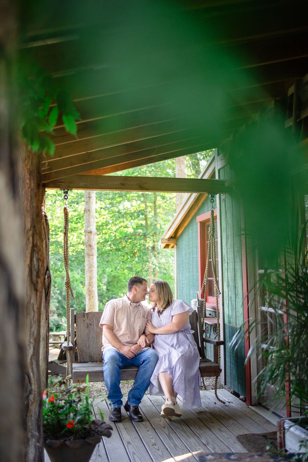 Couple sitting close together on rustic wooden porch surrounded by greenery.