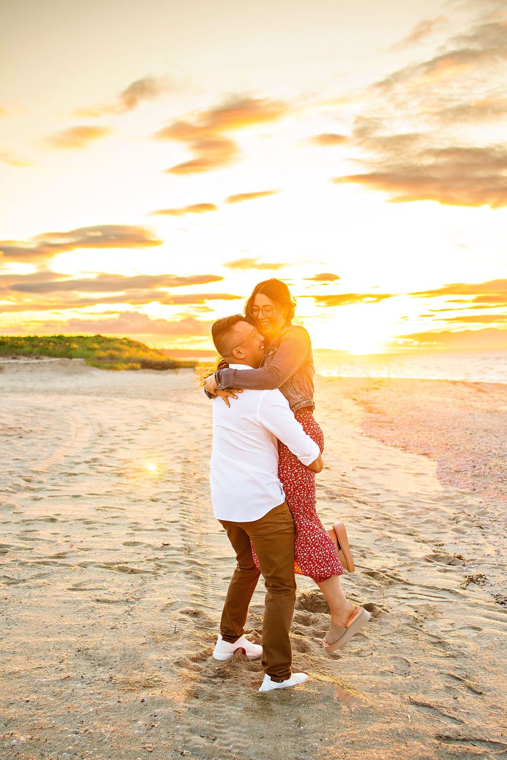 Couple embracing on beach at golden sunset with waves and dramatic sky in background.
