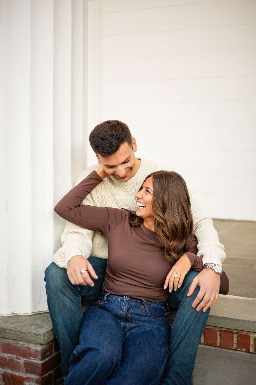 A couple sits together on a porch, sharing intimate laughter and embraces in a casual setting.