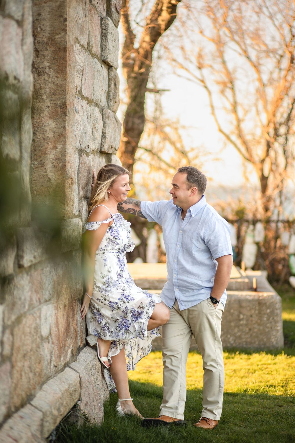 Romantic couple poses against stone wall during golden hour outdoors.