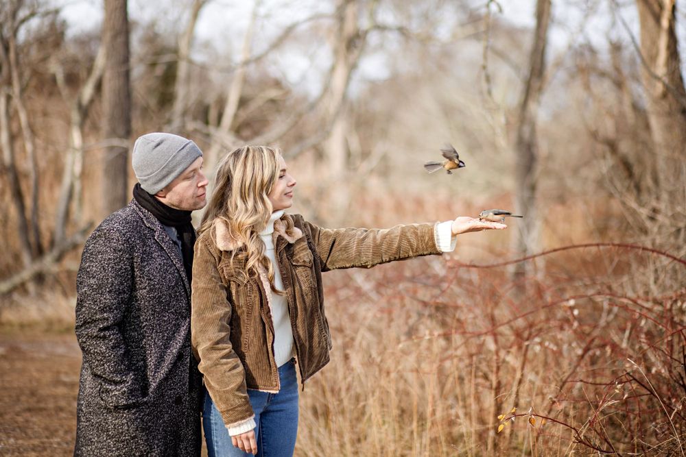 A couple points at something in the distance while standing among autumn brush.