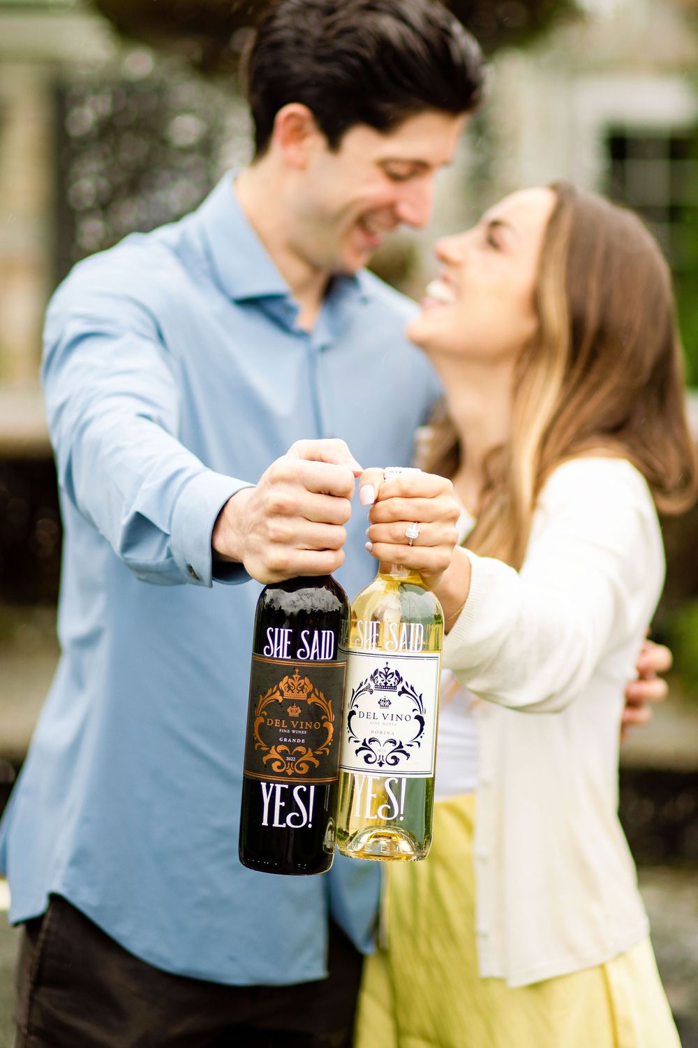 A couple shares an intimate moment while displaying wine bottles labeled 'Yes' in an outdoor setting.