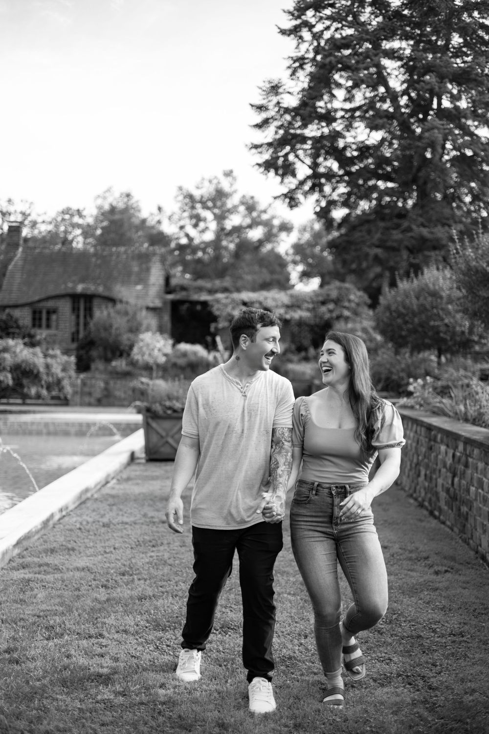 Laughing couple walking together through a lush garden in black and white photo.