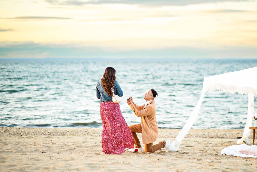 Romantic beach proposal scene with couple on sandy shore at sunset with ocean view.