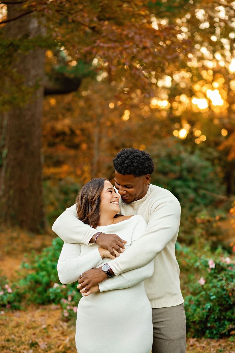 A romantic couple embraces outdoors during golden hour in an autumn forest setting.