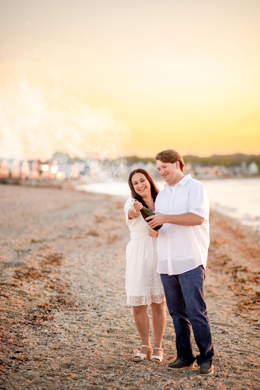 A couple laughs while looking at something on their phone during a beach photoshoot.