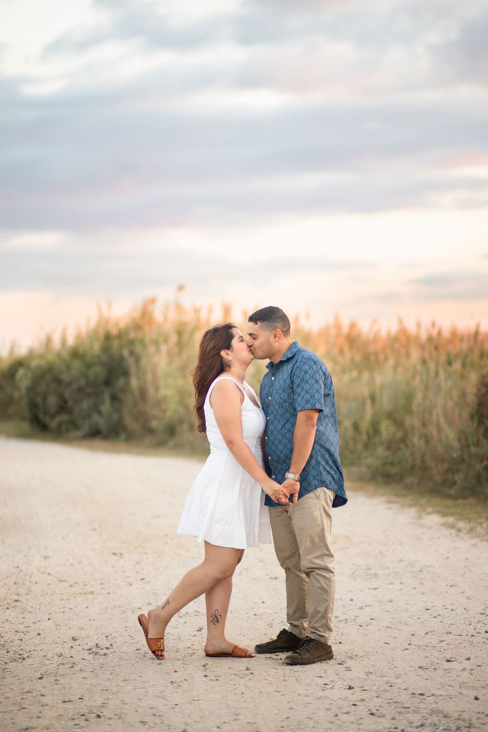Romantic couple in casual attire sharing an intimate moment on a sandy beach path at sunset.