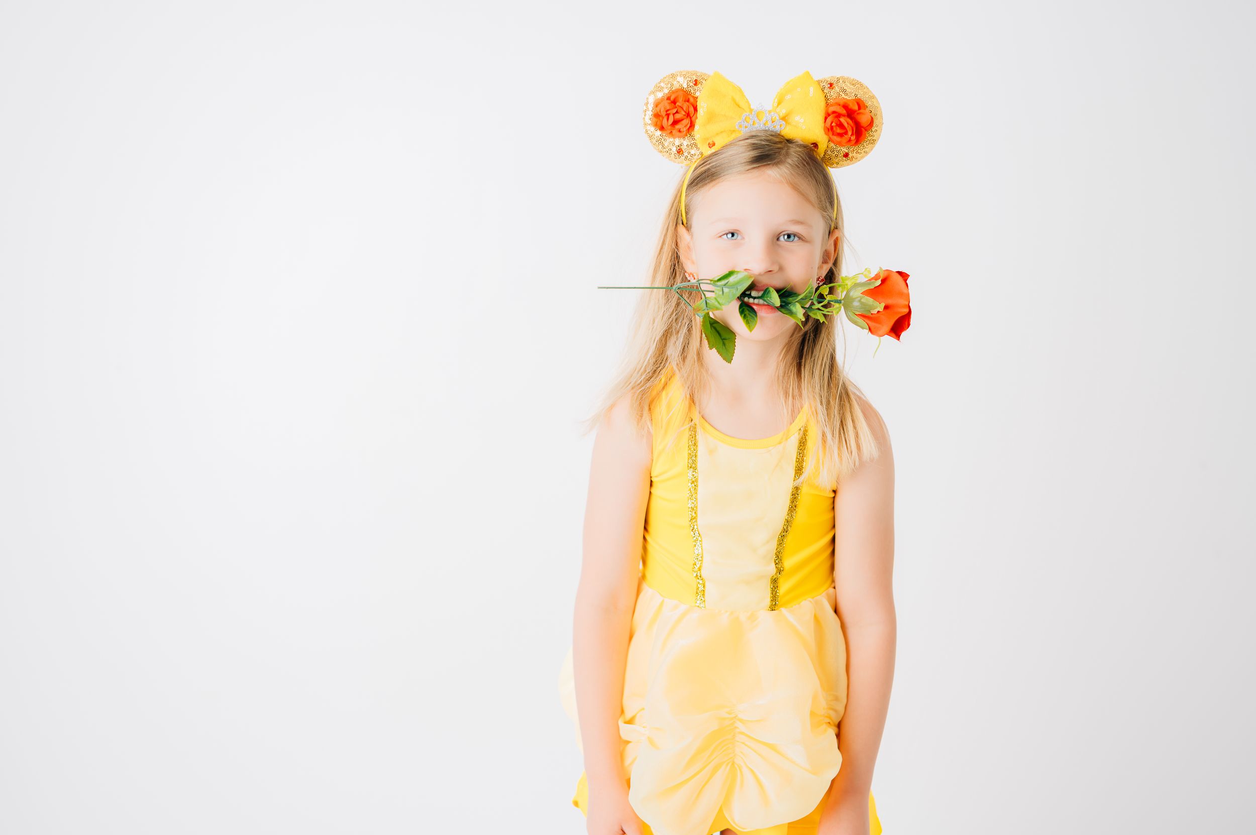 A child in a yellow dress wearing orange flower decorations poses against a white background.