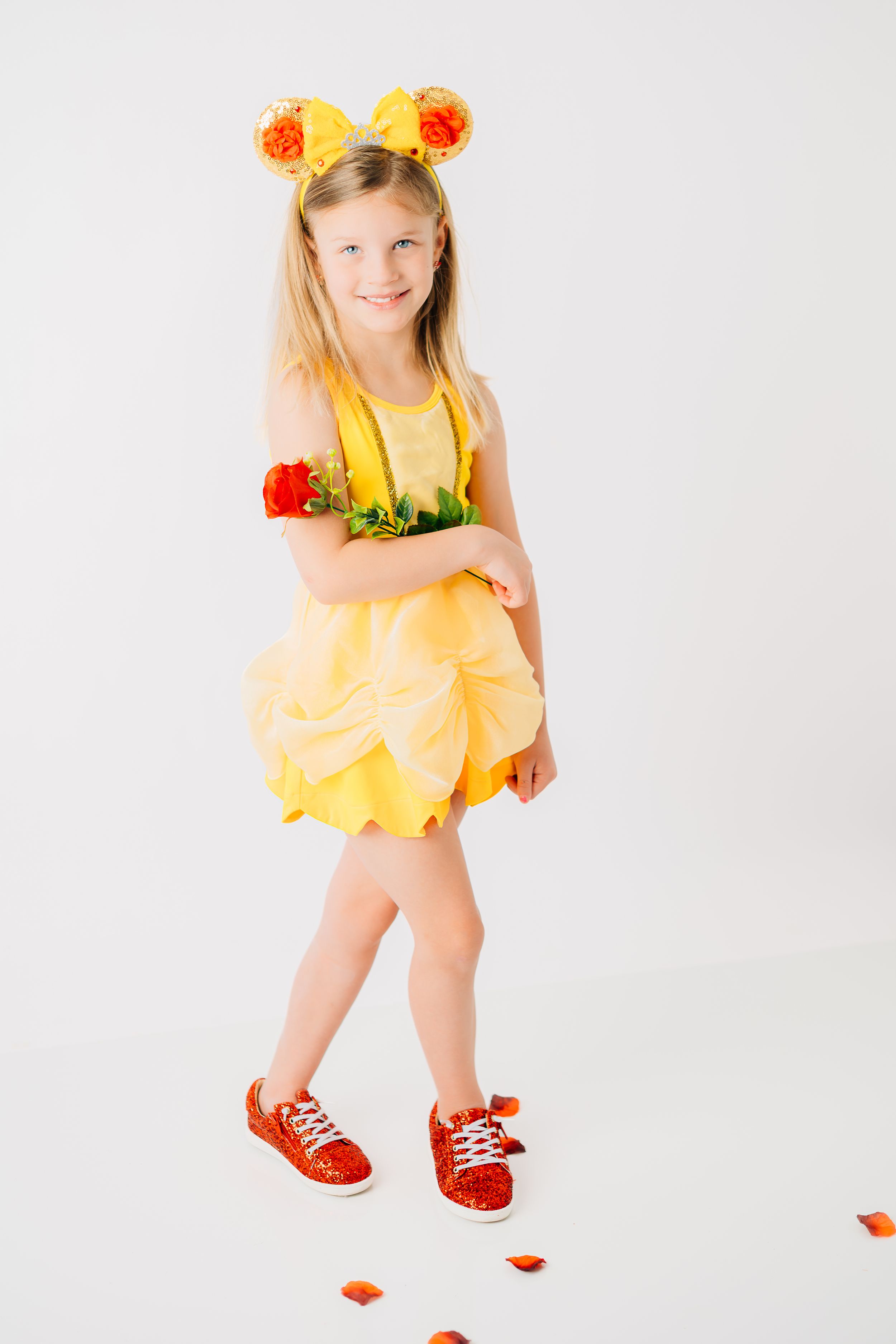Whimsical yellow dress costume with floral mouse ears and red sneakers against white background.