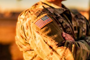 Close-up of American flag patch on military camouflage uniform in golden sunlight.